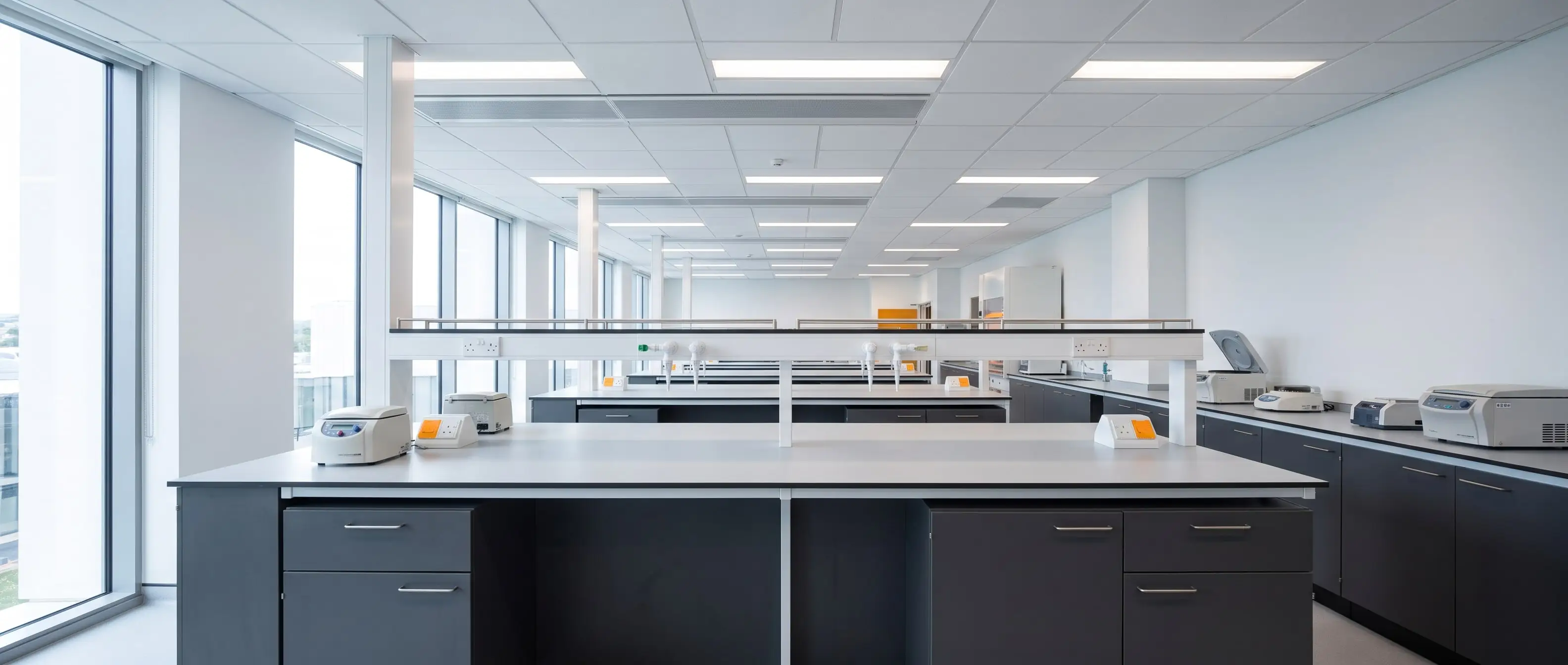 Perspective row of graphite laboratory benches with pale worktops in bright even light